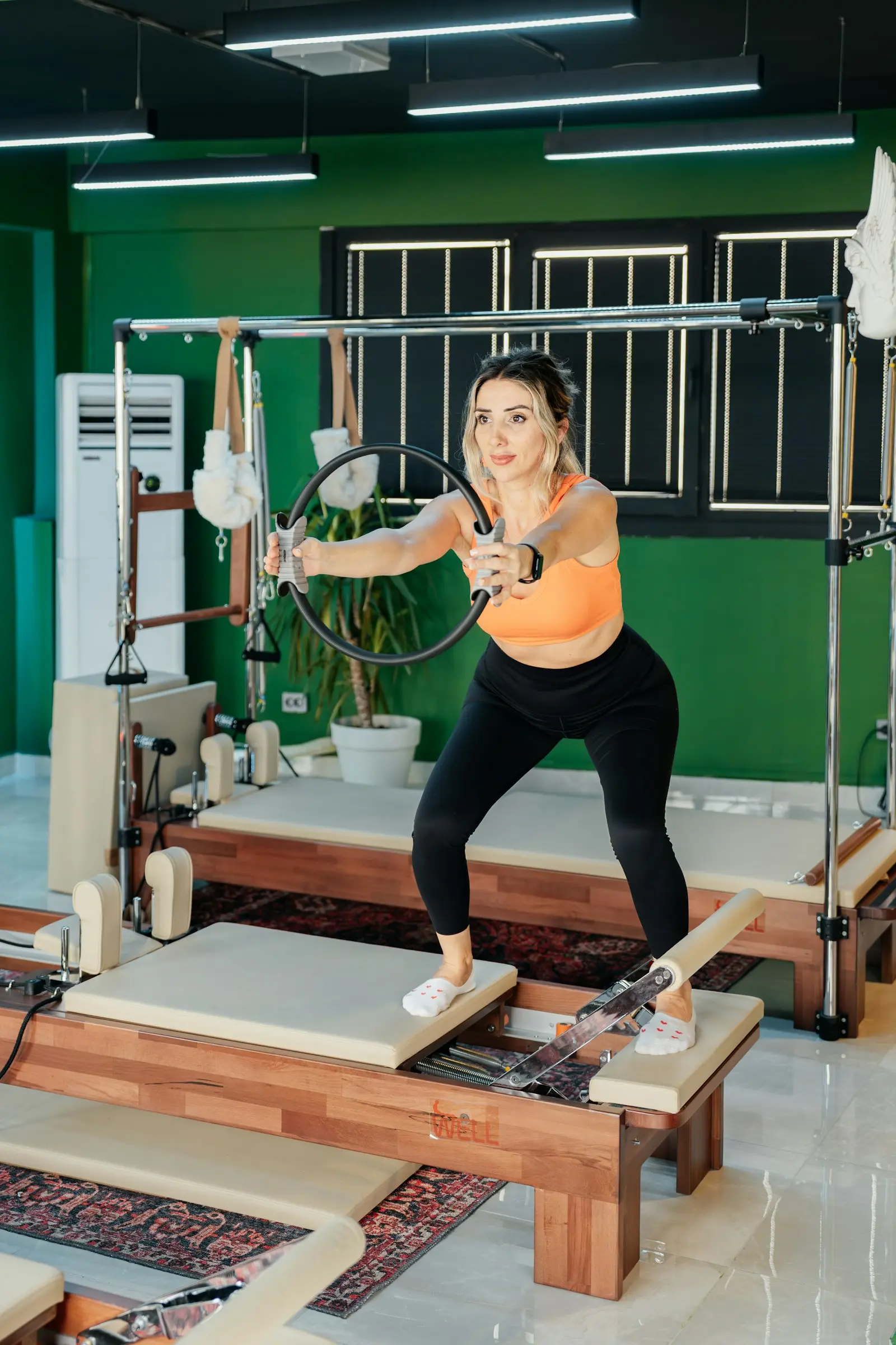 Femme en tenue orange qui fait une fente avec les poignées d’un Reformer