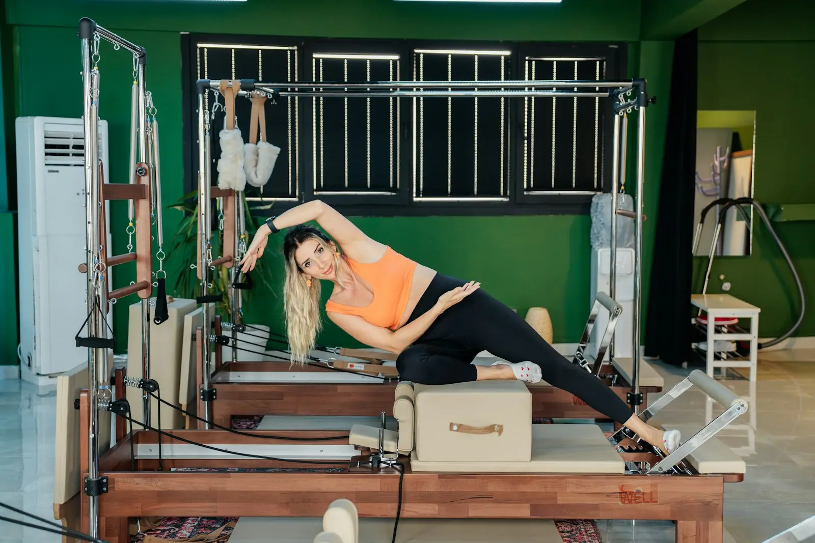 Femme en étirement latéral sur un Reformer, dans un studio aux murs verts