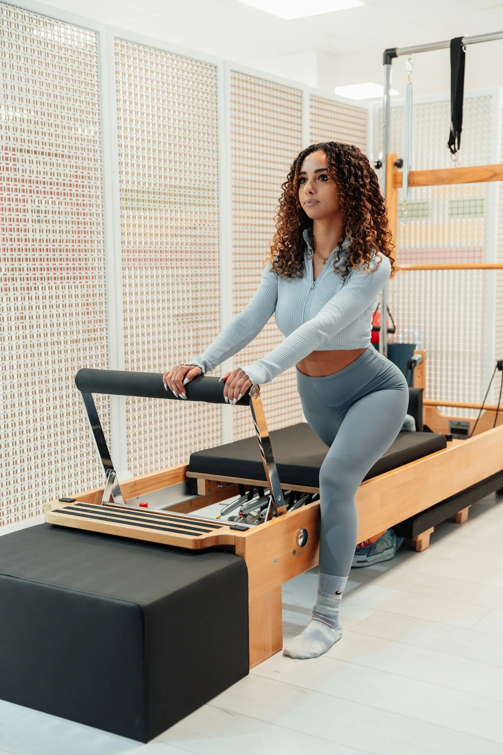 Femme debout sur un Reformer, un genou plié, les mains sur la barre