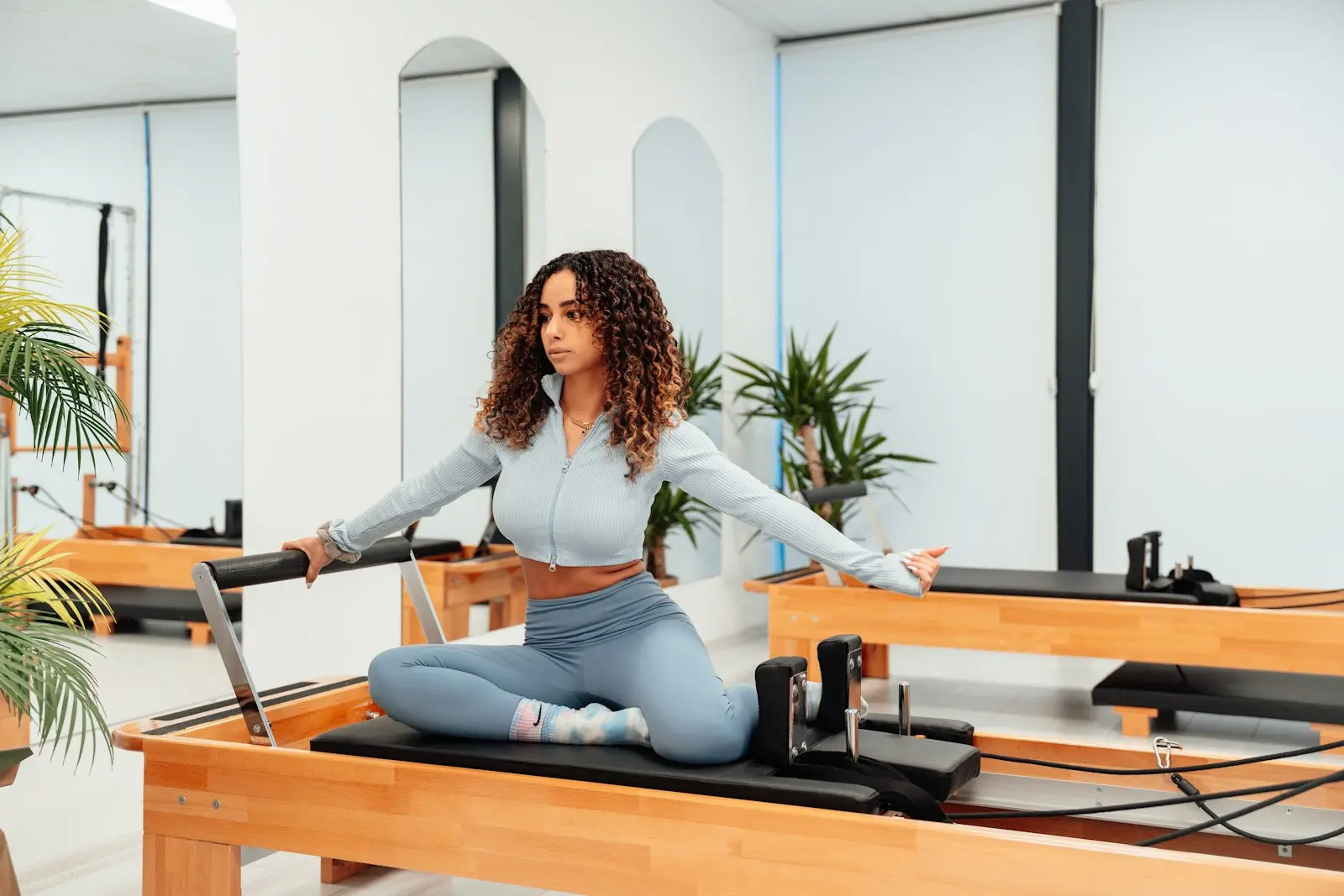 Femme assise sur un Reformer, bras tendus vers l’avant, dans un studio lumineux